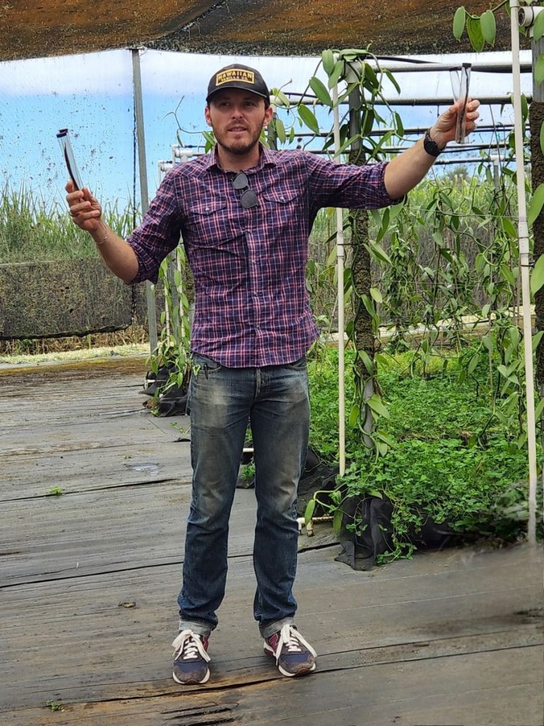 Hawaiian Vanilla Company tour guide and operations manager Bryce Hackney, in the vanilla shadehouse, demonstrating the difference between two USDA approved vanilla pods and two non-approved varietal pods. Photo by Karen Alman 